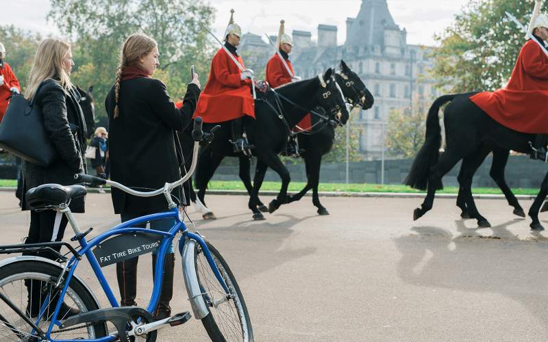 Two bicyclists taking a picture of royal guards on horses