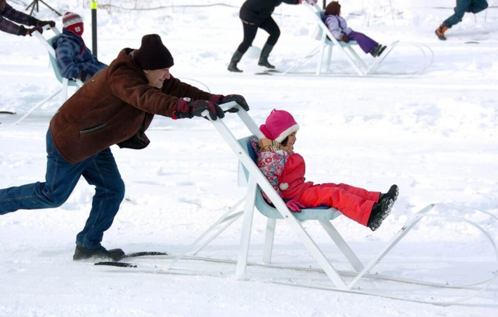 A dad pushing his daughter on a sled in la fete des neiges