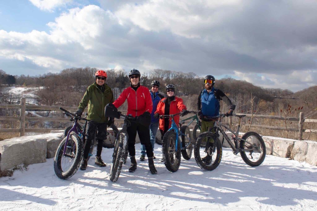 group of cyclists at sweet pete's in toronto posing in front of evergreen brickworks winter scenery