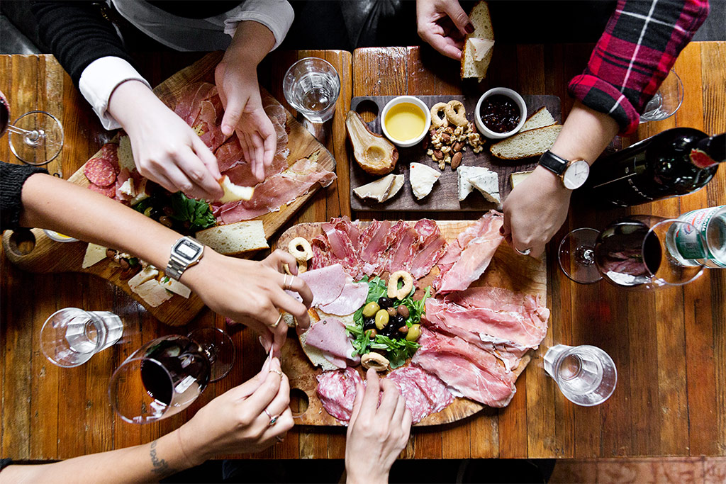 Group of people sharing charcuterie boards accompanied with wine on a wooden table 